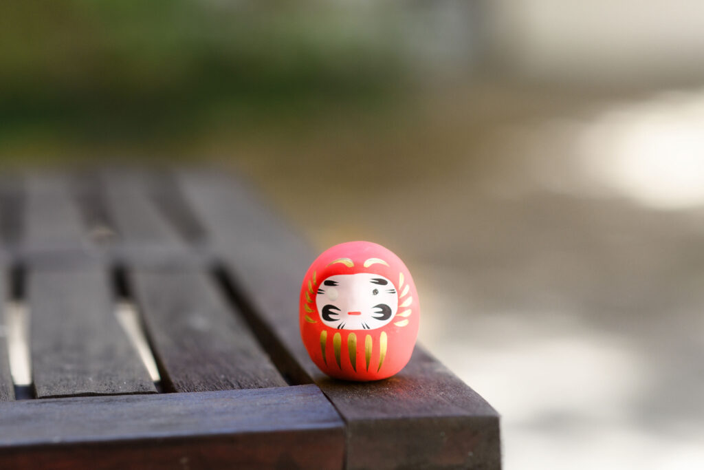 Rote Daruma-Figur auf einer Holzbank als Symbol für Zielklarheit und Durchhaltevermögen.